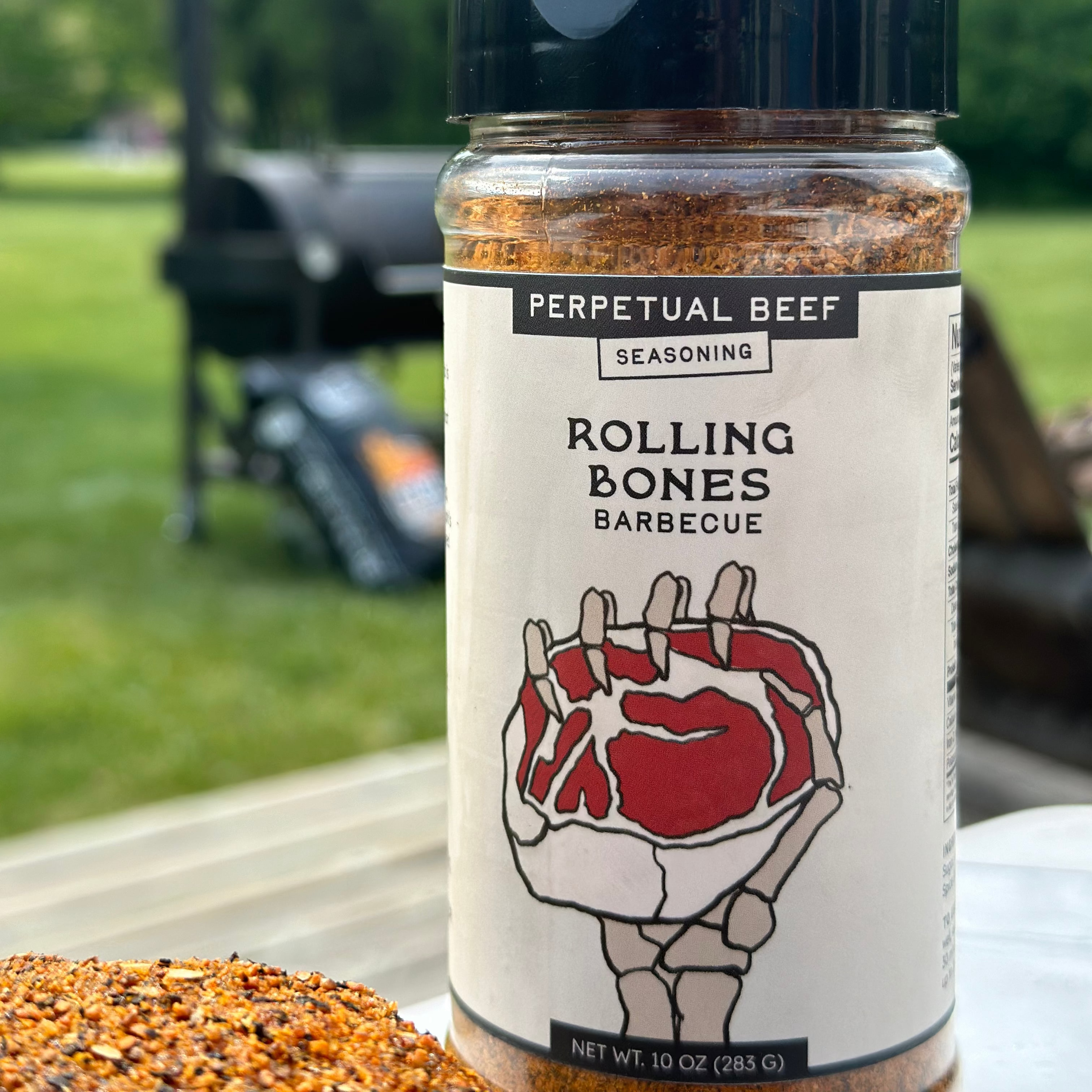 A plastic jar of Rolling Bones Barbecue Perpetual Beef dry rub with a label that features a hand holding a steak, with a background suggestive of an outdoor grilling setting.