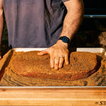 Bottle of Rolling Bones BBQ Perpetual Beef dry rub seasoning on a brisket.