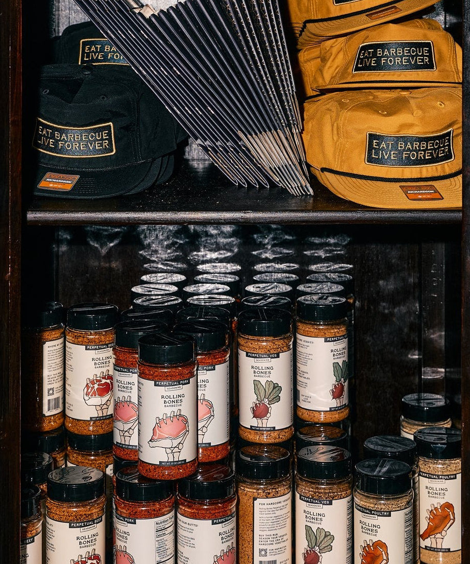 Shelf with Rolling Bones barbecue products including dry rubs, BBQ hats, and boxes.
