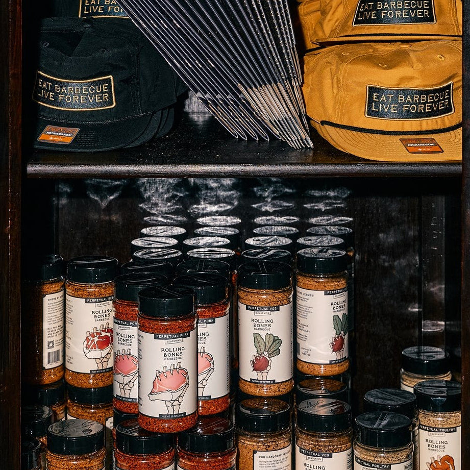 Shelf with Rolling Bones barbecue products including dry rubs, BBQ hats, and boxes.