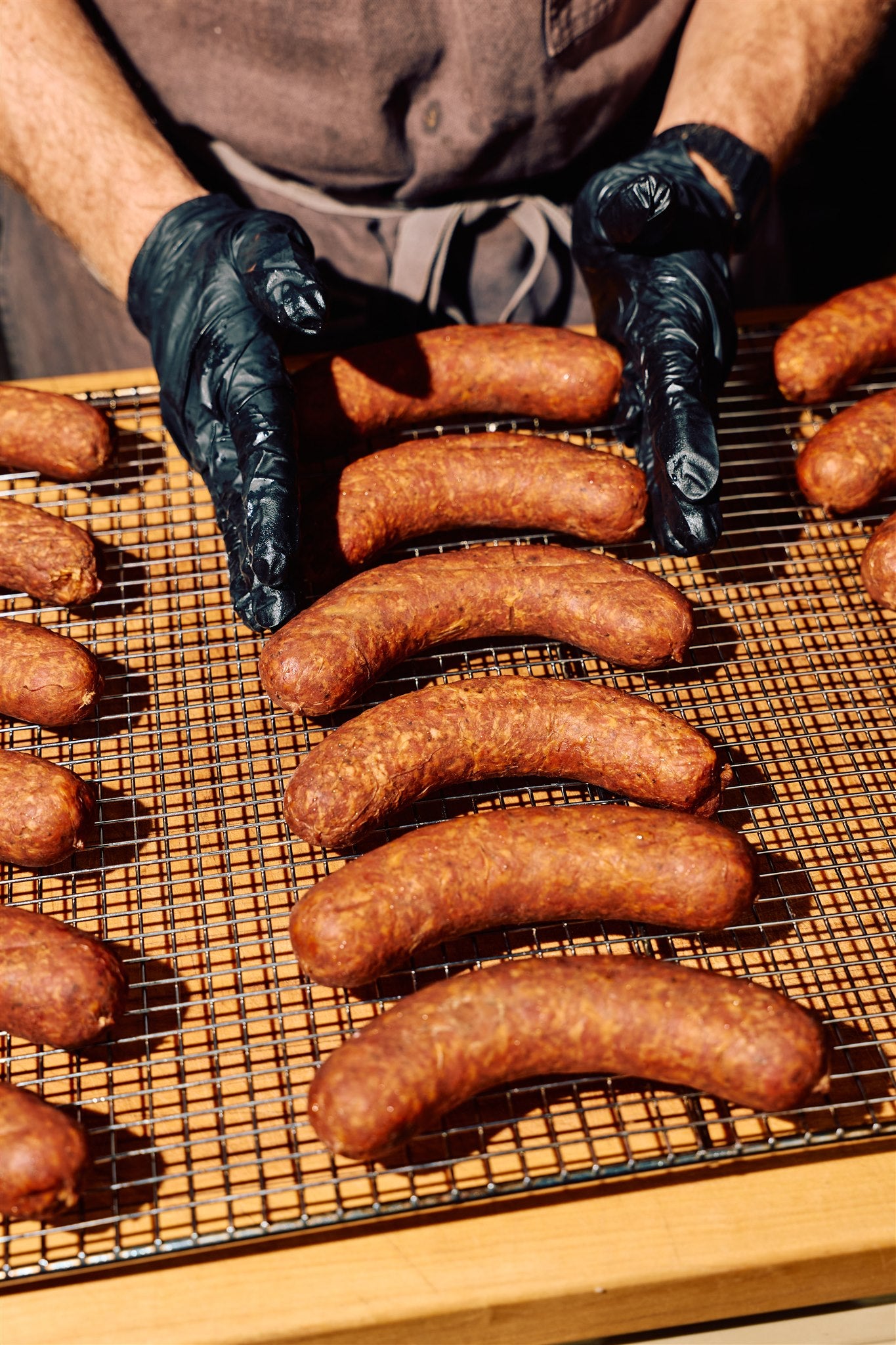 Will from Rolling Bones BBQ proudly showing off perfectly smoked sausages on a wire rack for guests for a barbecue gathering.