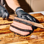 Bottle of Rolling Bones BBQ Perpetual Beef dry rub seasoning forming the bark on a sliced brisket.